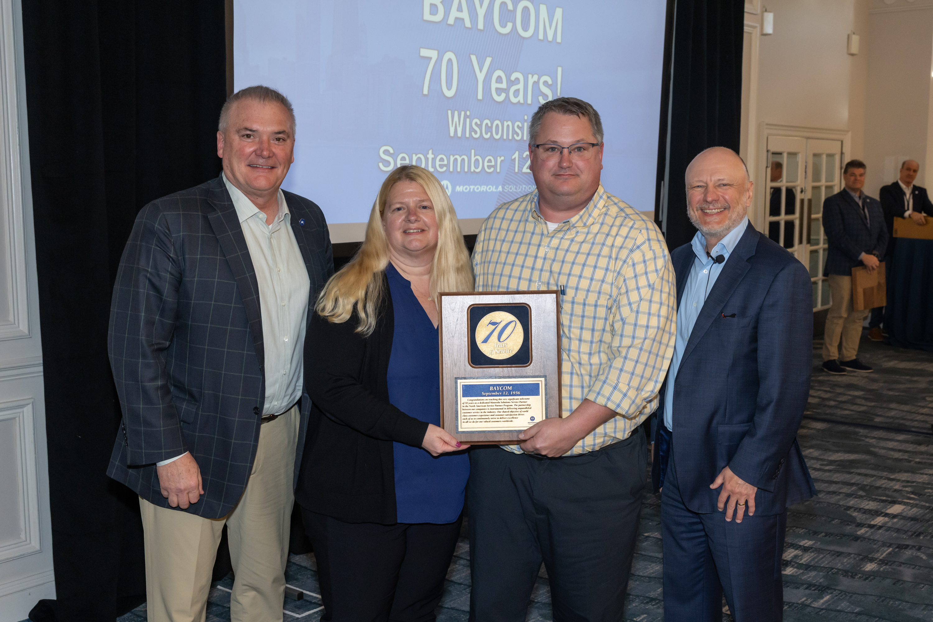 4 people holding plaque in front of screen